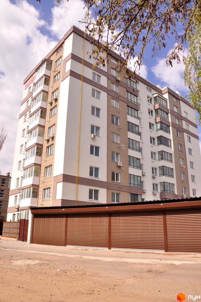 Зовнішній вигляд новобудови ЖК Мирний з коричневими елементами та балконами. На прибудинковій території розташовані гаражні ворота.