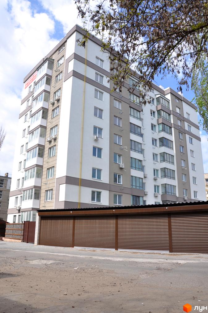 Зовнішній вигляд новобудови ЖК Мирний з білими та сірими фасадами, заскленими балконами та коричневими ролетними воротами на прибудинковій території.