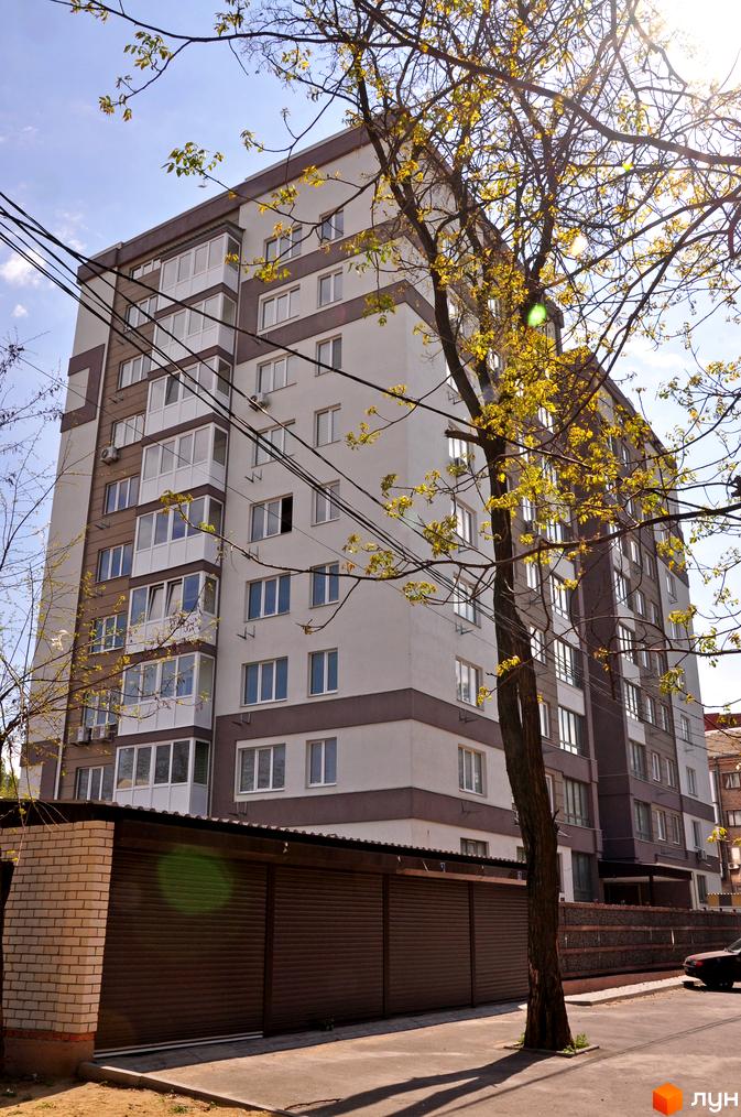 Зовнішній вигляд багатоповерхового будинку ЖК Мирний з балконами та вікнами. На передньому плані видно гаражні ворота та дерево.