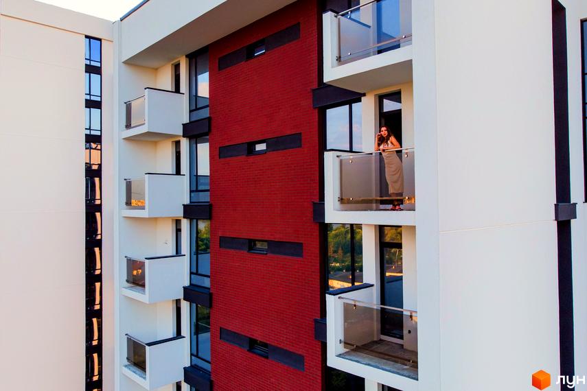 Житловий район Manhattan. Сучасна архітектура житлового комплексу з червоною цегляною стіною та скляними балконами. Зовнішній вигляд будівлі.