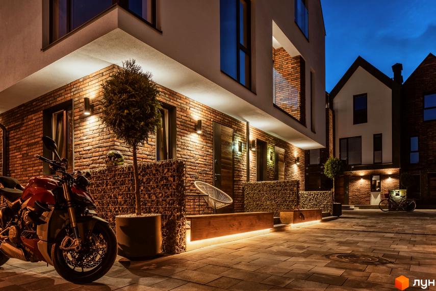 Зовнішній вигляд котеджного містечка КМ Wunder Haus з цегляним фасадом та підсвічуванням. На прибудинковій території розташовані мотоцикл та велосипед.