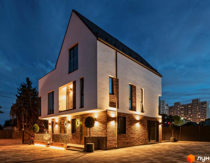 Котеджне містечко КМ Wunder Haus з цегляним фасадом та білими стінами ввечері. Прибудинкова територія освітлена ліхтарями.