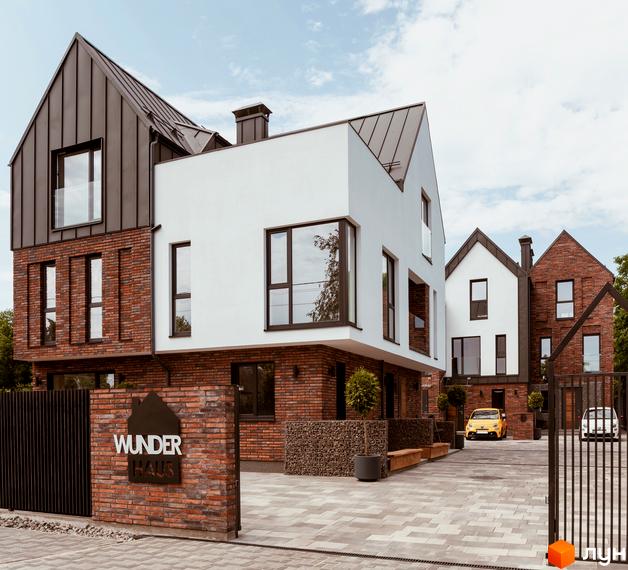 Котеджне містечко Wunder Haus: фасади з цегли та білої штукатурки, металевий дах, прибудинкова територія з бруківкою та жовтим авто.