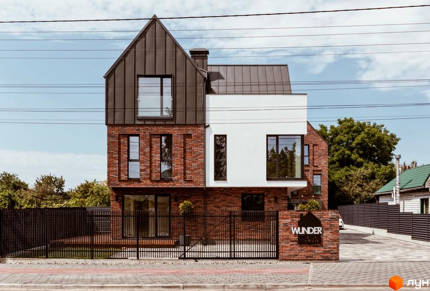 Котеджне містечко Wunder Haus: двоповерховий будинок з цегляним та білим фасадом, великими вікнами та металевим дахом. Огороджена територія з парканом та воротами.