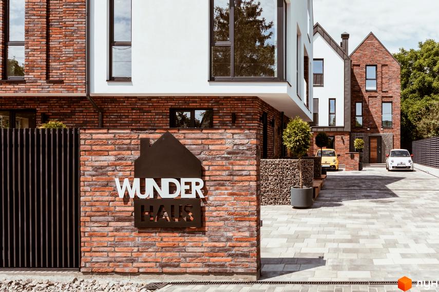 Котеджне містечко Wunder Haus з цегляним фасадом та білою обробкою, парковка з автомобілями та зелені насадження.