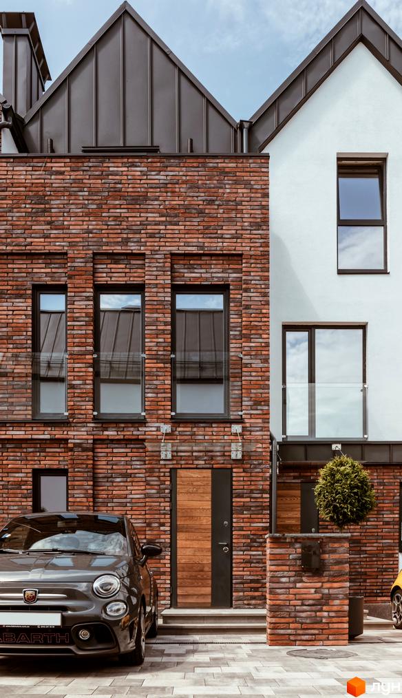 Котеджне містечко КМ Wunder Haus: фасади з червоної цегли та білої штукатурки, великі вікна, дерев'яні двері, сірий автомобіль біля будинку.