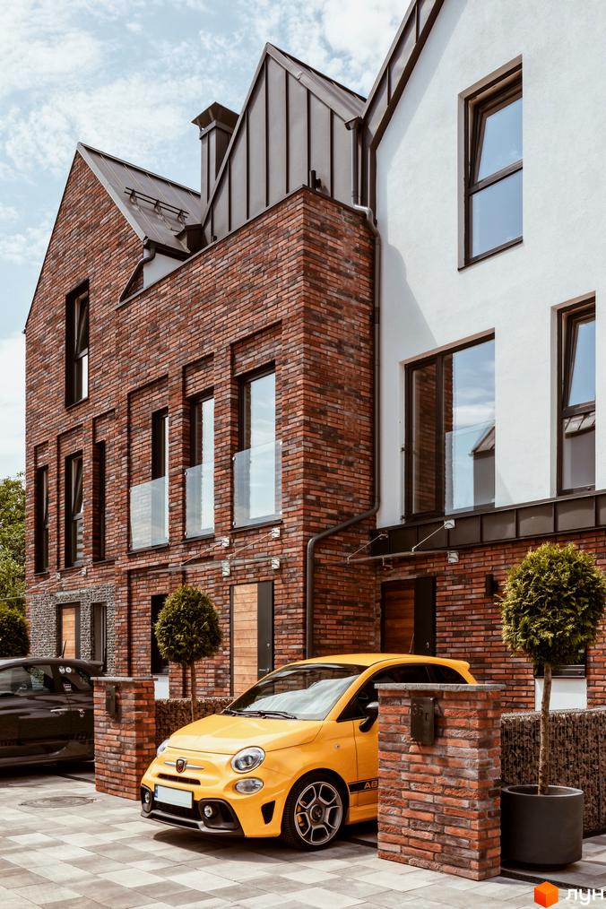 КМ Wunder Haus - котеджне містечко з цегляними фасадами та білими стінами, поруч жовтий автомобіль та зелені дерева.