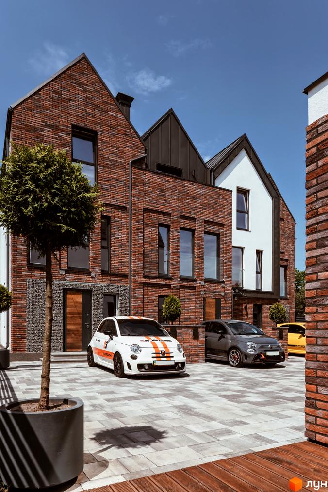 Котеджне містечко КМ Wunder Haus з цегляним фасадом та прибудинковою територією з бруківки. На території розташовані автомобілі та зелені насадження.