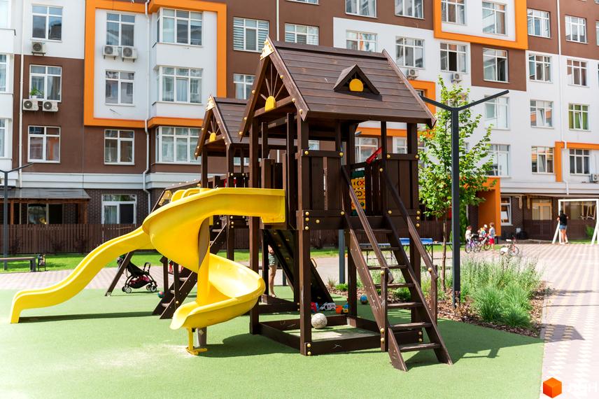 Житловий комплекс Orange Park з дитячим майданчиком та гірками. Навколо будівель розташована зелена зона та доріжки для прогулянок.