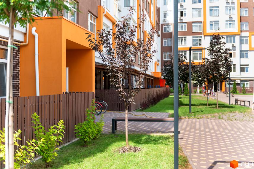 Житловий комплекс Orange Park: фасади будівель поєднують оранжевий та коричневий кольори. Територія облаштована зеленими зонами, парканом та місцями для відпочинку.