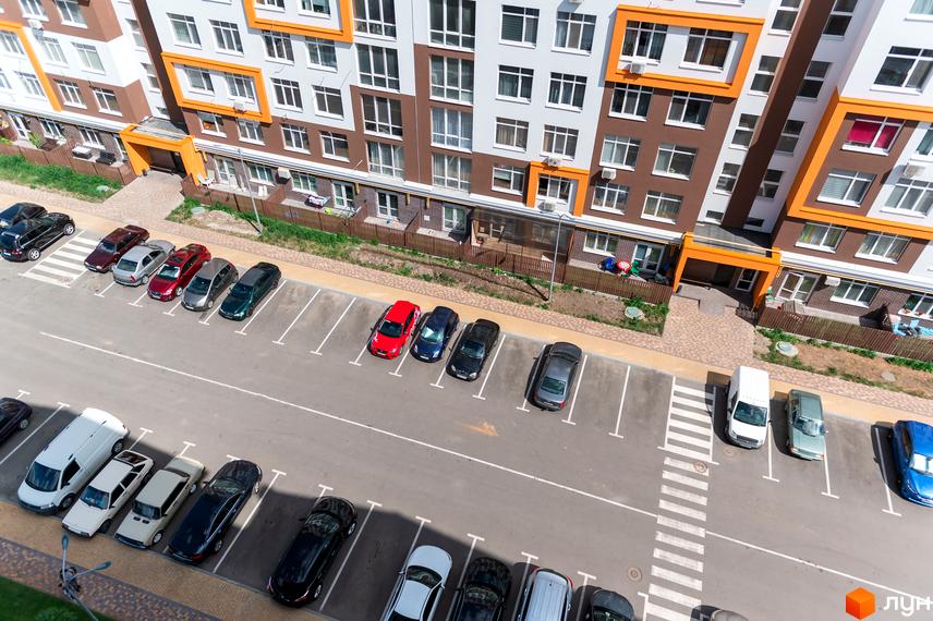 Новобудова ЖК Orange Park з коричнево-білим фасадом та оранжевими елементами. На прибудинковій території розташована парковка з автомобілями.