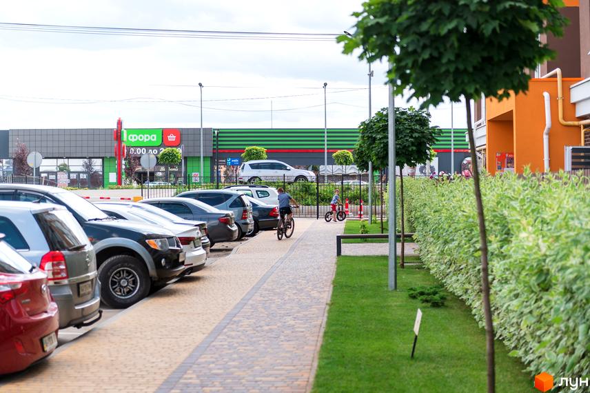 Житловий комплекс Orange Park. Парковка біля новобудови з фасадом помаранчевого кольору. Поруч доглянута прибудинкова територія з газоном та деревами.