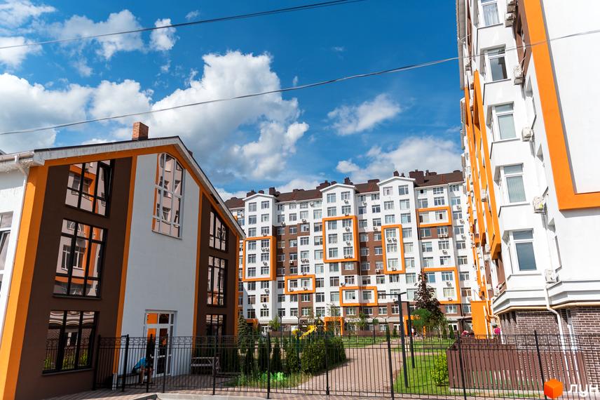 Житловий комплекс Orange Park: фасади будівель з помаранчевими елементами, вікна, кондиціонери. Прибудинкова територія з газоном та деревами.