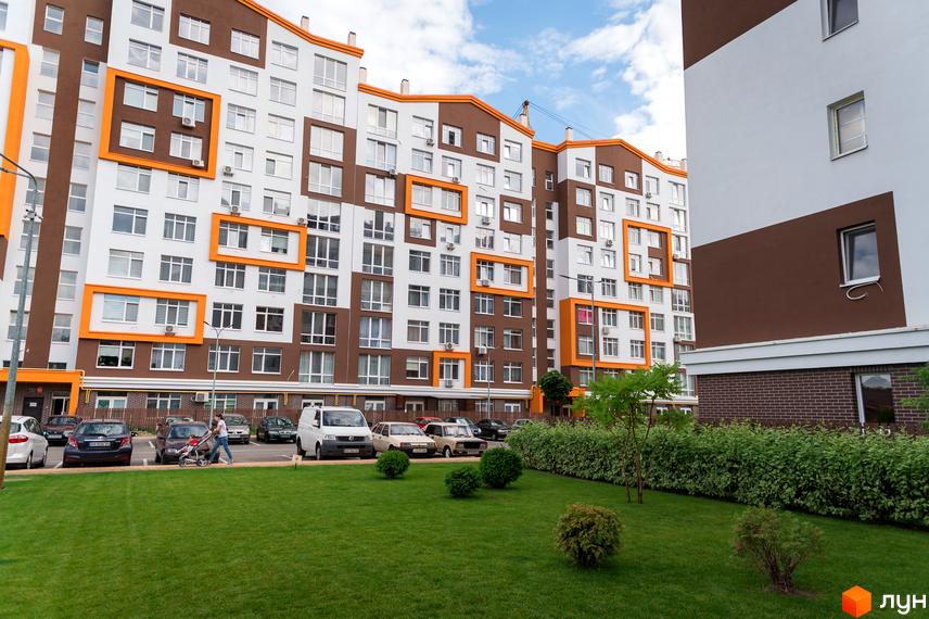 Житловий комплекс Orange Park з коричнево-білими фасадами та помаранчевими акцентами. На прибудинковій території доглянутий газон та кущі.