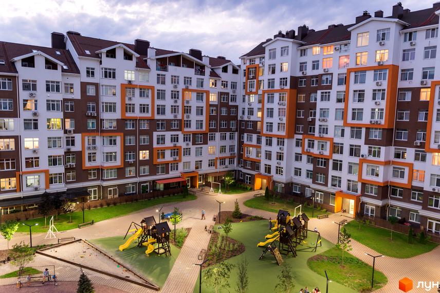 Житловий комплекс Orange Park з коричнево-білими фасадами та оранжевими акцентами. На прибудинковій території дитячий майданчик з гірками та пісочницею.