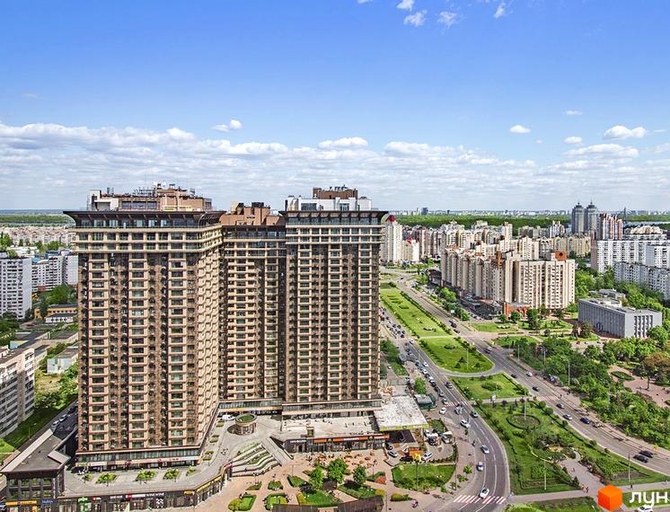 Житловий комплекс Obolon Residences складається з двох високих будівель світло-коричневого кольору. Навколо комплексу видно зелені зони, дороги з автомобілями та інші будинки.