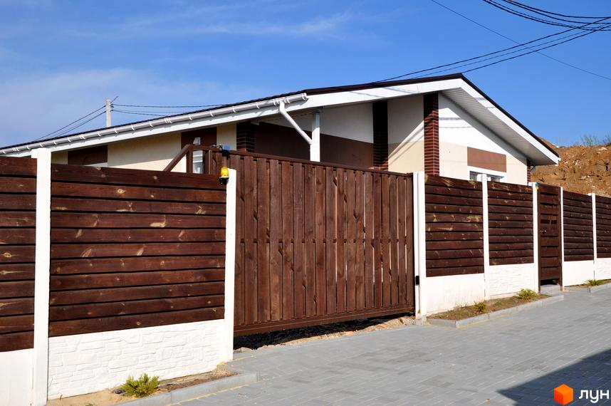 Котеджне містечко КМ Данилівський: будинок з коричневим дерев'яним парканом та воротами, білі бетонні стовпи, сіра бруківка.