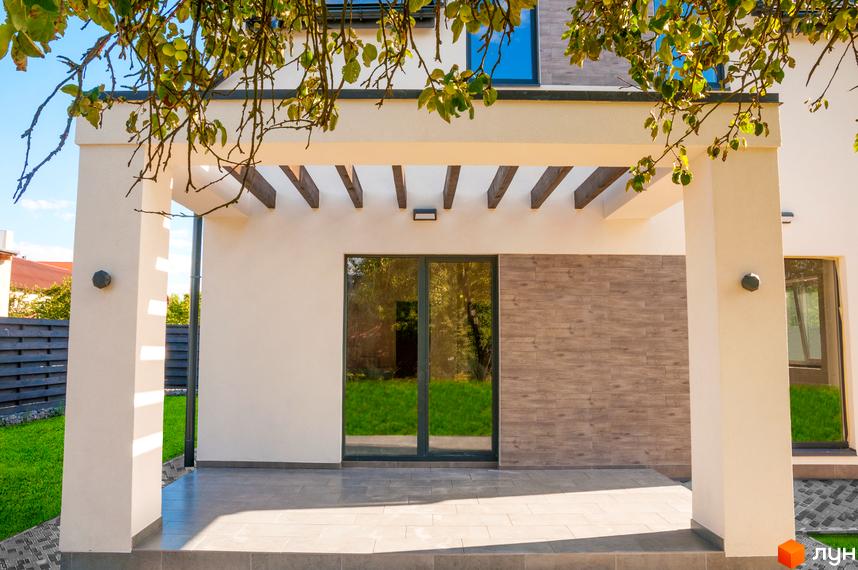 Зовнішній вигляд будинку з терасою та великим вікном, що виходить на зелену галявину. Котеджне містечко Романкiвська Мрiя.