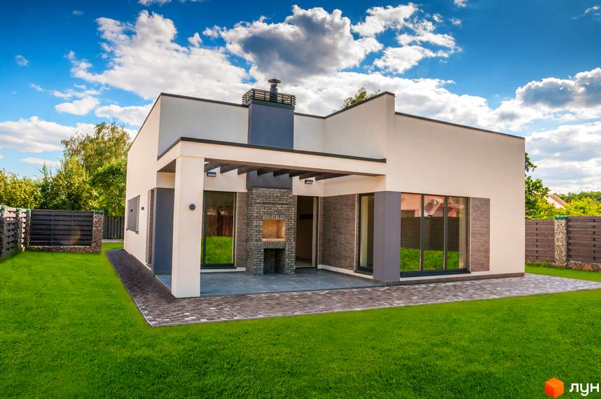 Одноповерховий будинок з великими вікнами та піччю на терасі. Зелена галявина перед будинком та кам'яний паркан.