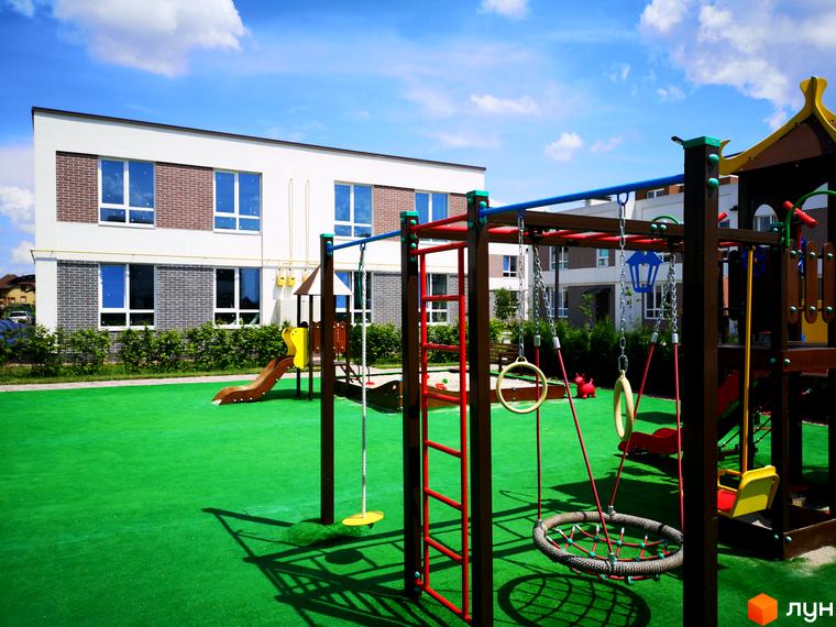 Сучасний житловий комплекс Country Townhouse з дитячим майданчиком. Будівля має цегляний фасад та великі вікна. Територія навколо будинку вкрита зеленим газоном.