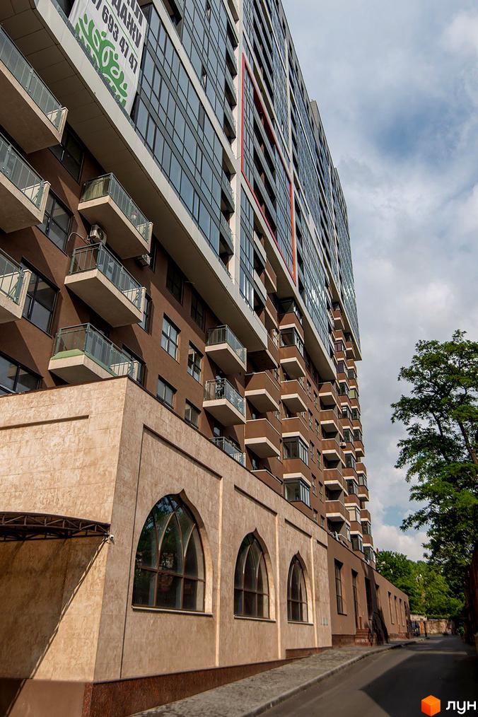 Новобудова ЖК Баку з коричневим фасадом, скляними балконами та арочними вікнами. Зовнішній вигляд будинку та частина прибудинкової території.