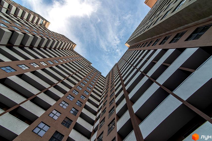 Вигляд знизу на висотний житловий комплекс Баку з численними балконами та вікнами. Фасад будівлі коричневого кольору з білими елементами.