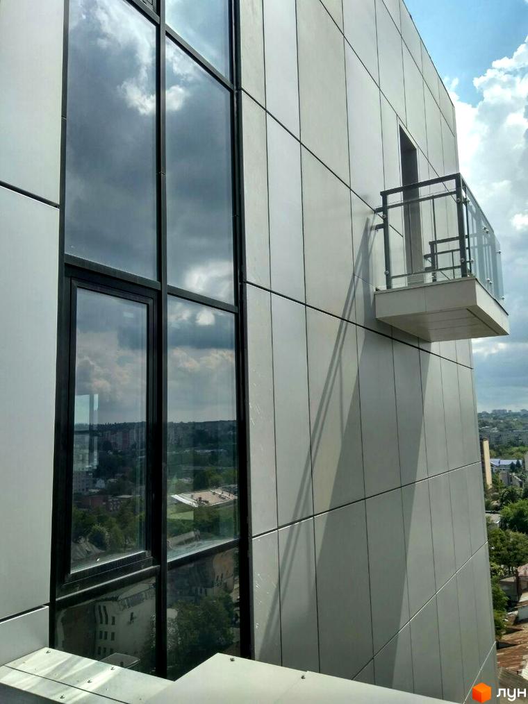 Фасад житлового комплексу Баку з великими вікнами та балконом, що відображають хмари. Навколо видно міський пейзаж із зеленню.