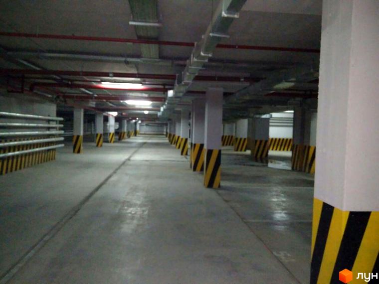 Підземний паркінг у житловому комплексі Баку з колонами, захищеними чорно-жовтими смугами. Просторий паркінг з бетонною підлогою та стелею.