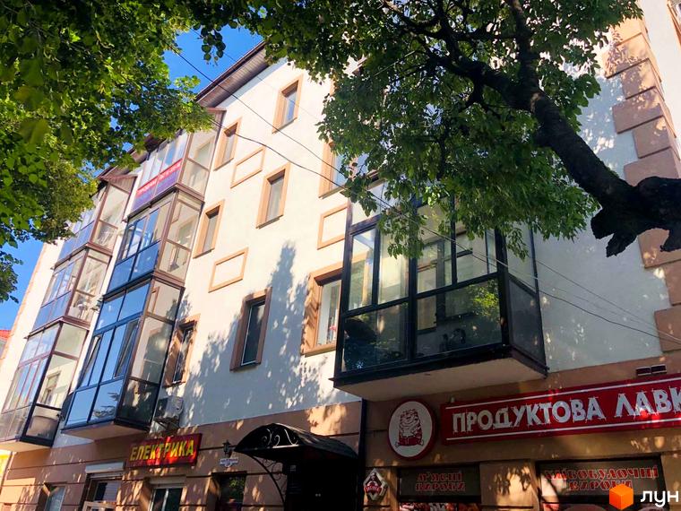 Фасад житлового комплексу на вул. Петра Могили, 28, з заскленими балконами та деревами на передньому плані.