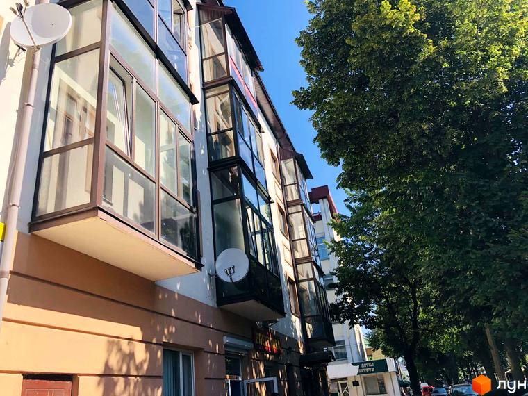 Зовнішній вигляд будинку на вул. Петра Могили, 28, з заскленими балконами та зеленими деревами поруч. Опис новобудови для просування сайту.