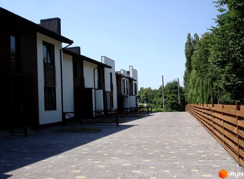 Зовнішній вигляд новобудови на вулиці Князя Острозького, 3б, з бруківкою та дерев'яним парканом.