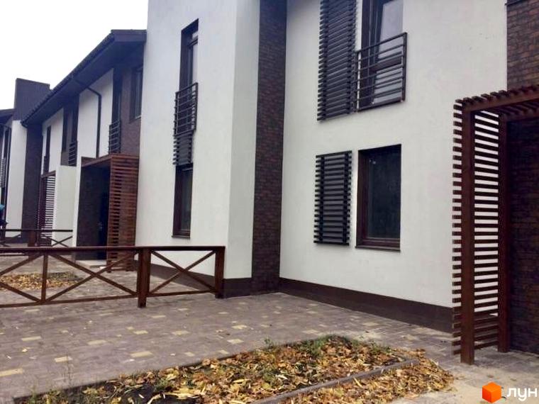 Зовнішній вигляд новобудови на вул. Князя Острозького, 3б, з дерев'яним парканом та бруківкою на прибудинковій території.