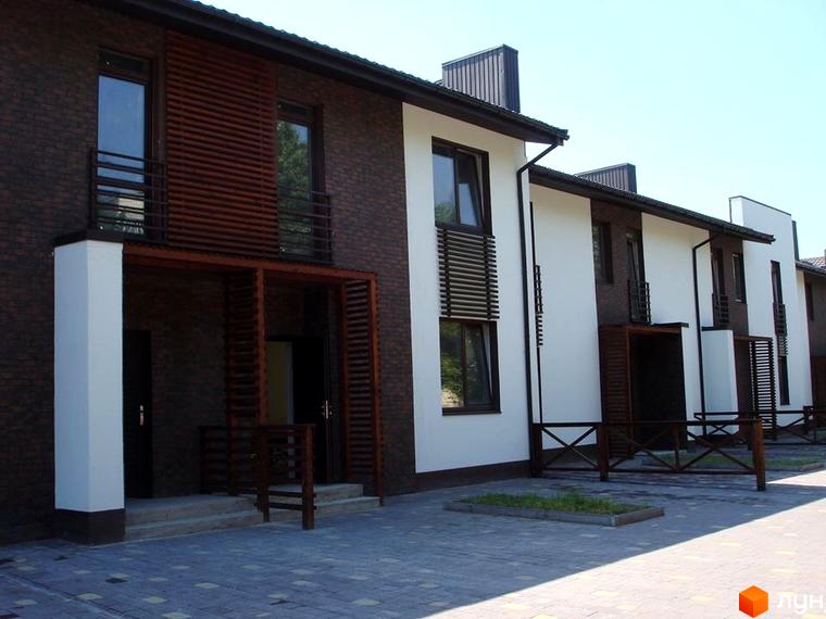 Зовнішній вигляд новобудови на вул. Князя Острозького, 3б, з цегляним фасадом та дерев'яними елементами. Прибудинкова територія вимощена плиткою.