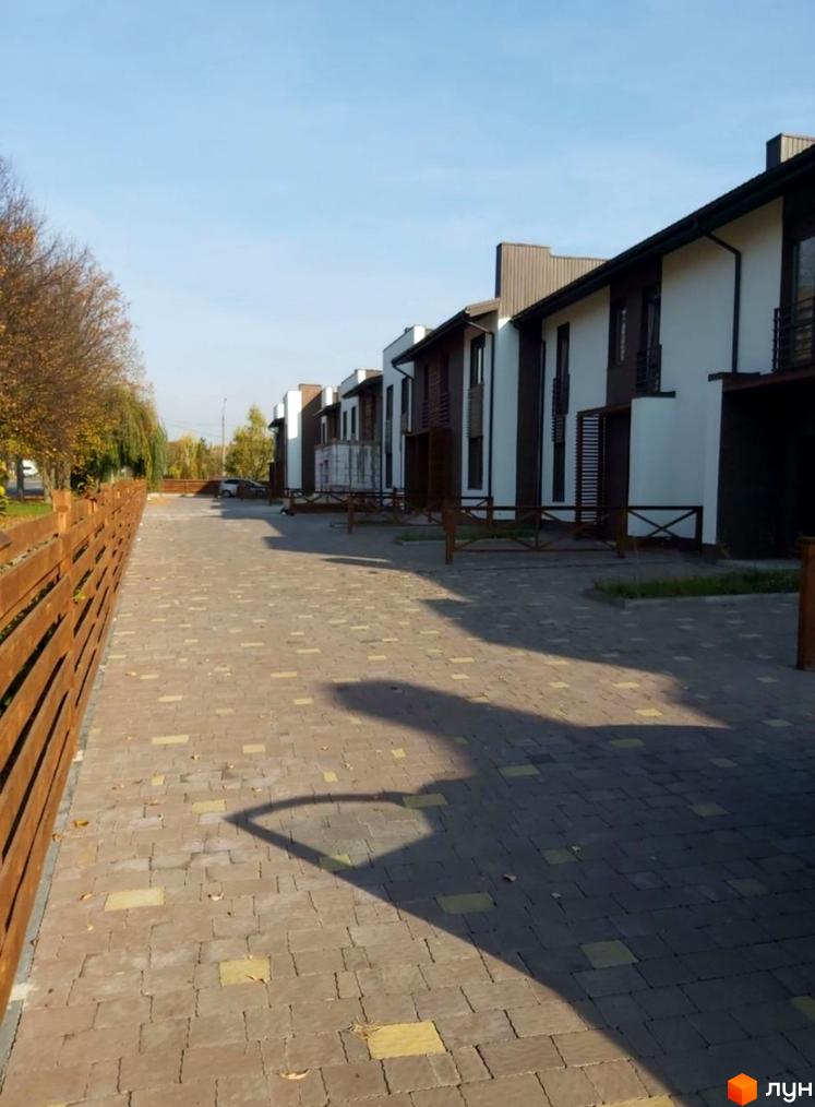 Зовнішній вигляд будинків житлового комплексу на вул. Князя Острозького, 3б, з брукованою прибудинковою територією та дерев'яним парканом.