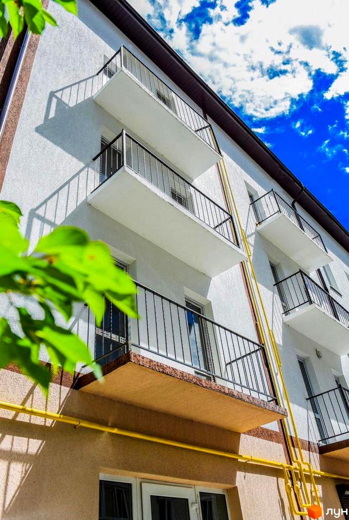 Зовнішній вигляд новобудови пров. Мирогощанський, 35 з балконами та вікнами на тлі блакитного неба з хмарами.