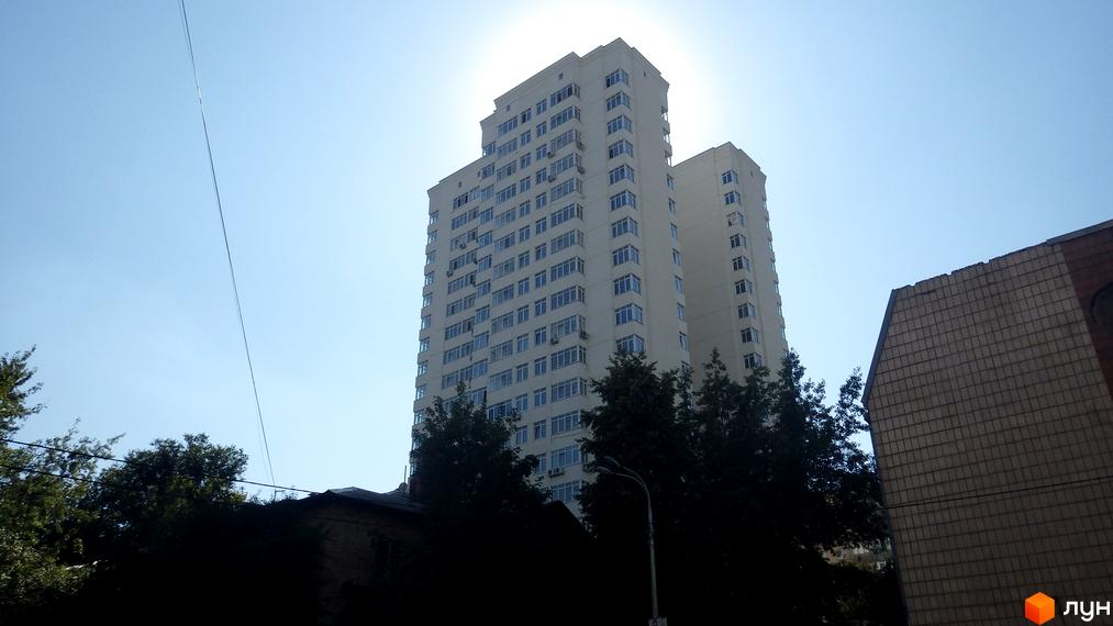 Висотний будинок житлового комплексу Затишний дім з великими вікнами та зеленими насадженнями на прибудинковій території.