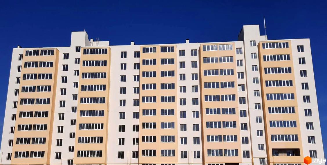 Вид на багатоповерховий житловий комплекс Морський (Южне) з численними вікнами та балконами на тлі синього неба. Новобудова має світло-бежевий та білий фасади.