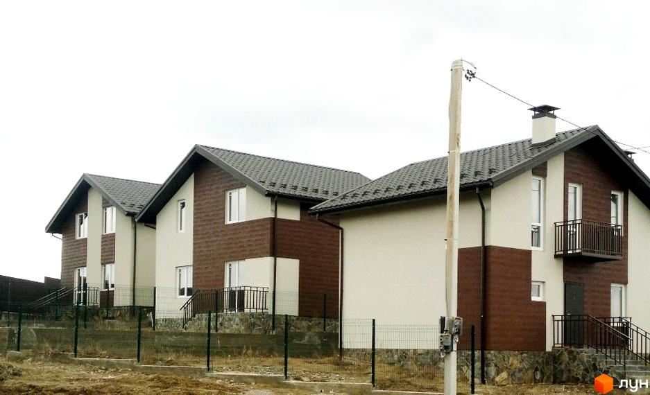 Котеджне містечко КМ Нова Конча-Заспа: двоповерхові будинки з коричневою та світлою обробкою фасадів, темними дахами та балконами. Територія огороджена парканом.