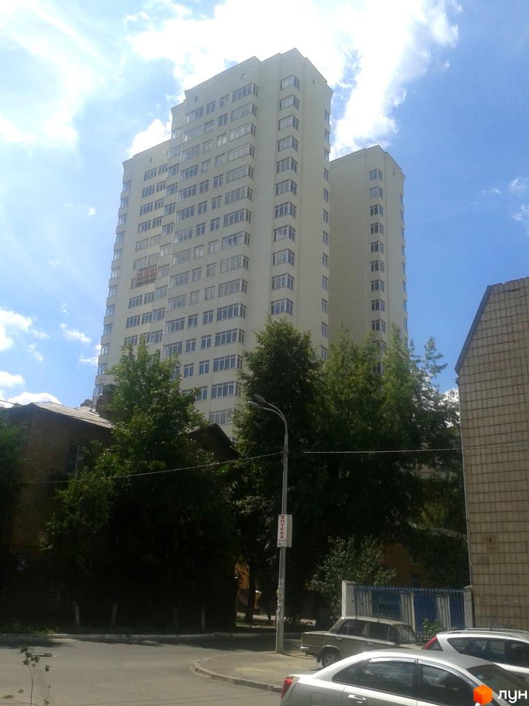 Висотний будинок житлового комплексу Затишний дім з великими вікнами. Прибудинкова територія з зеленими насадженнями та автомобілями.