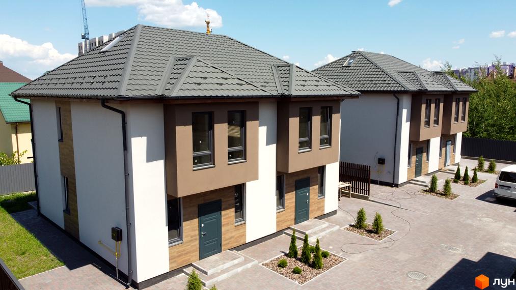 Дуплекси „На Вишгородській“: фасади будинків з коричневими та білими елементами, сірі дахи, бруківка та зелені насадження на прибудинковій території.