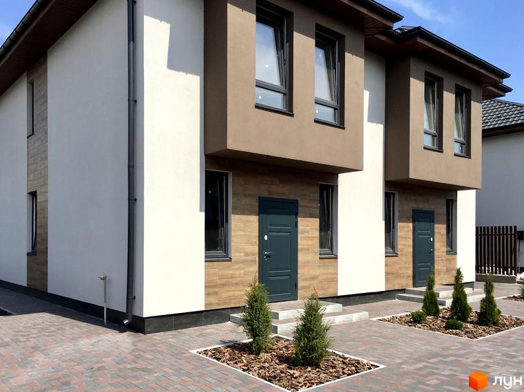 Дуплекси „На Вишгородській“: фасади будинків з білою та коричневою штукатуркою, дерев'яними вставками, темними дверима та вікнами. Прибудинкова територія вимощена плиткою, з доглянутими зеленими насадженнями.