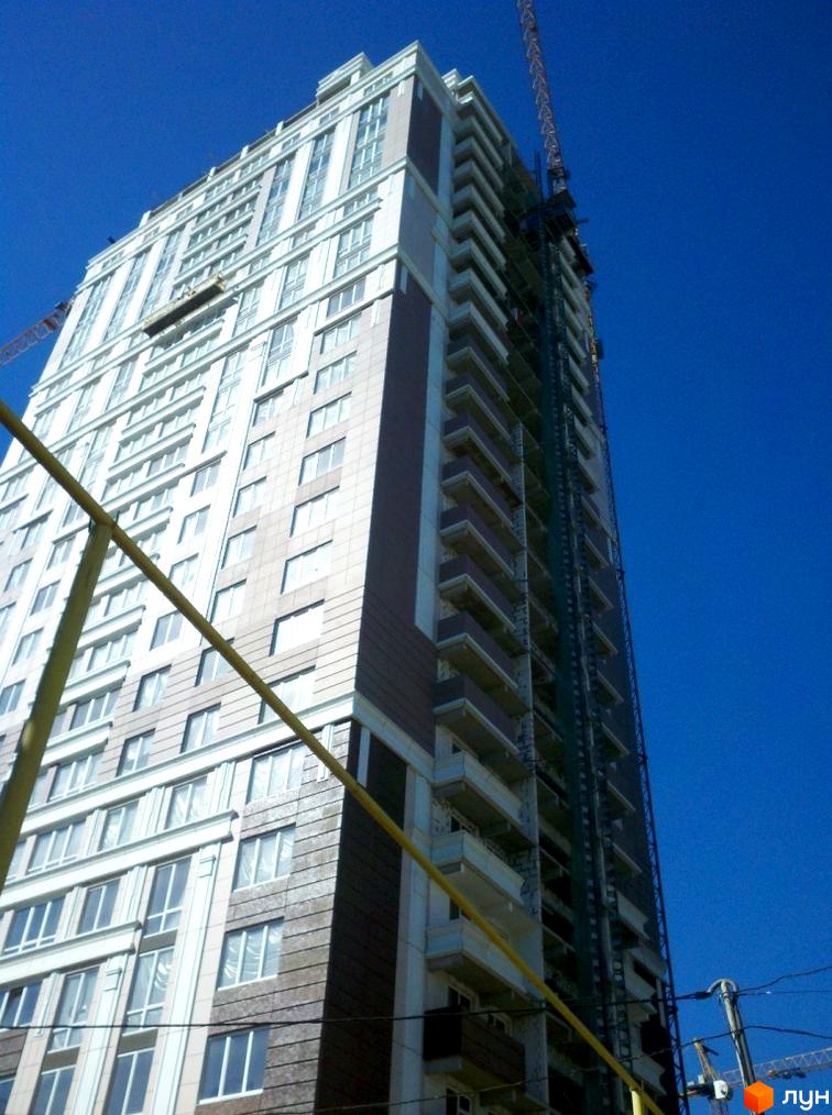 Високоповерховий житловий комплекс Гольфстрім з великою кількістю вікон та балконів. Будинок у світлих тонах з темними вставками, видно будівельний кран.