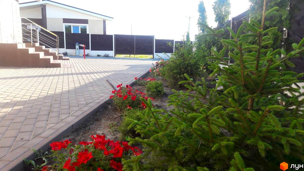 Котеджне містечко Данилівський: фасад будинку та ступінчатий вхід з металевим поручнем. Прибудинкова територія з бруківкою та квітами.