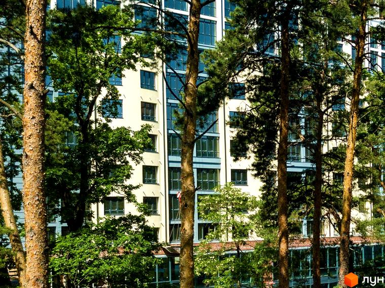 Житловий комплекс Royal Park: багатоповерхова будівля світлого кольору з великими вікнами, оточена густими зеленими деревами.