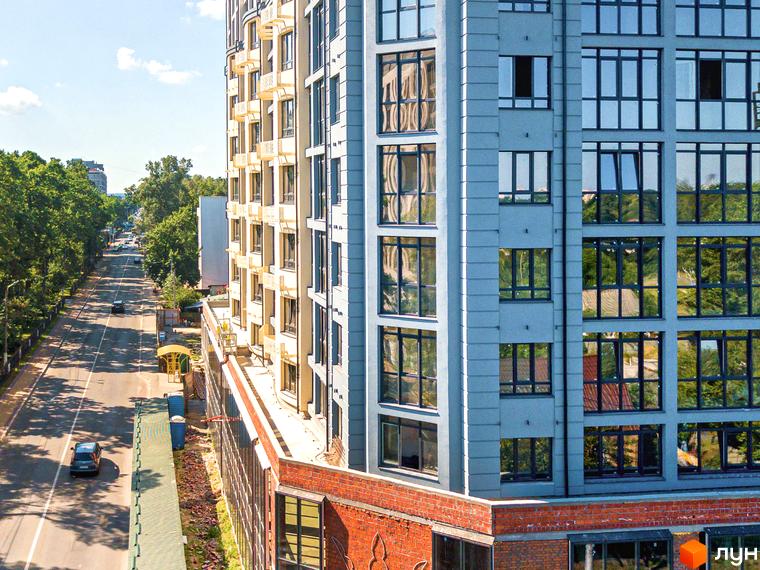 Багатоповерховий будинок Житлового комплексу Royal Park з великими вікнами та світлим фасадом, розташований біля широкої дороги, оточеної деревами.