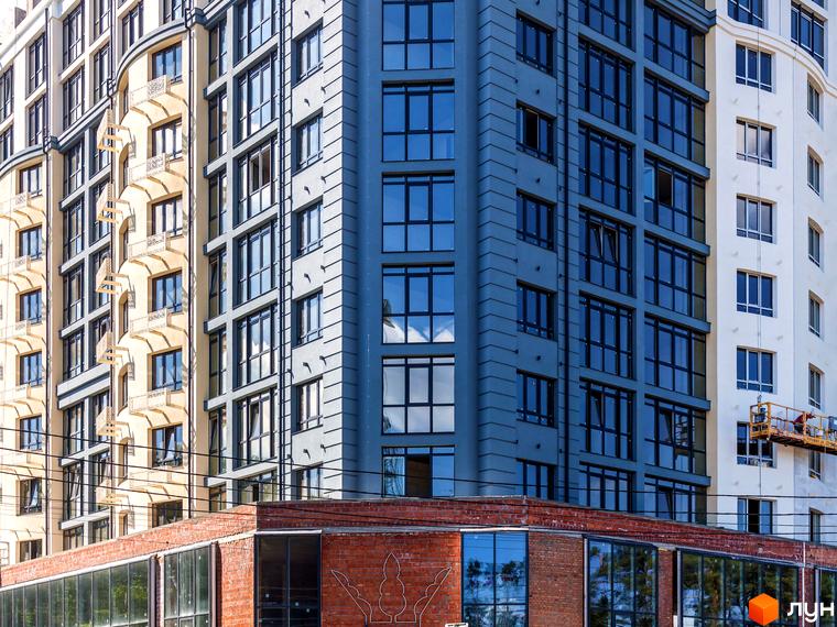 Висотна будівля ЖК Royal Park з великою кількістю вікон та фасадом у сірих тонах. На першому поверсі розташований цегляний будинок з панорамними вікнами.