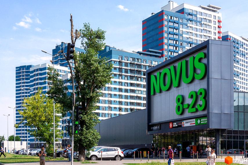 Житловий комплекс Галактика. Будинки з блакитними та білими фасадами, зелені насадження та парковка перед входом до супермаркету Novus.