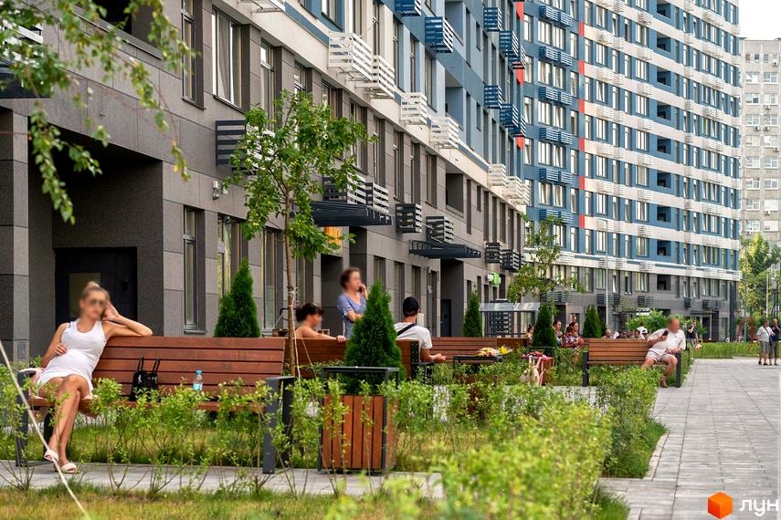 Житловий комплекс Галактика з сірими та блакитними фасадами та індивідуальними балконами. Прибудинкова територія з лавками, деревами та зеленими насадженнями.