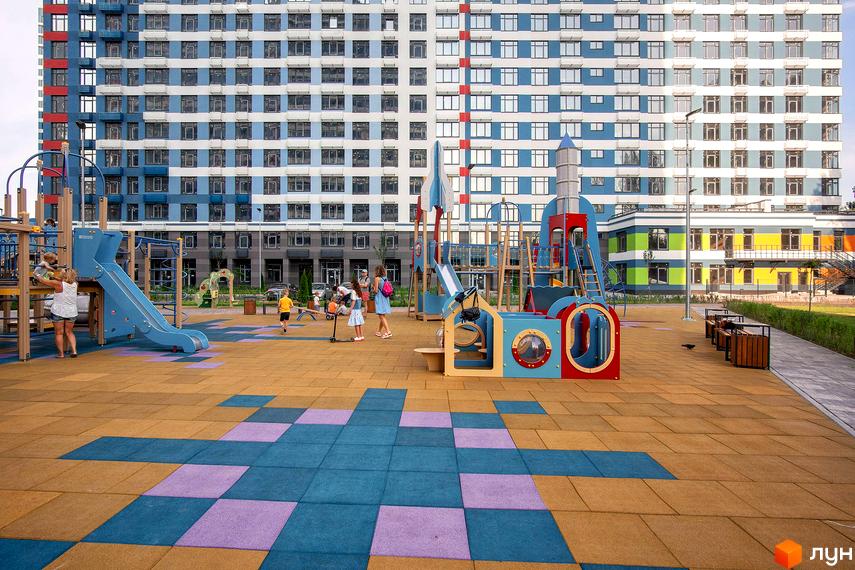 Житловий комплекс Галактика: фасади будівель у синьо-білих тонах та дитячий майданчик з гірками та гойдалками. Територія комплексу облаштована для відпочинку дітей та дорослих.
