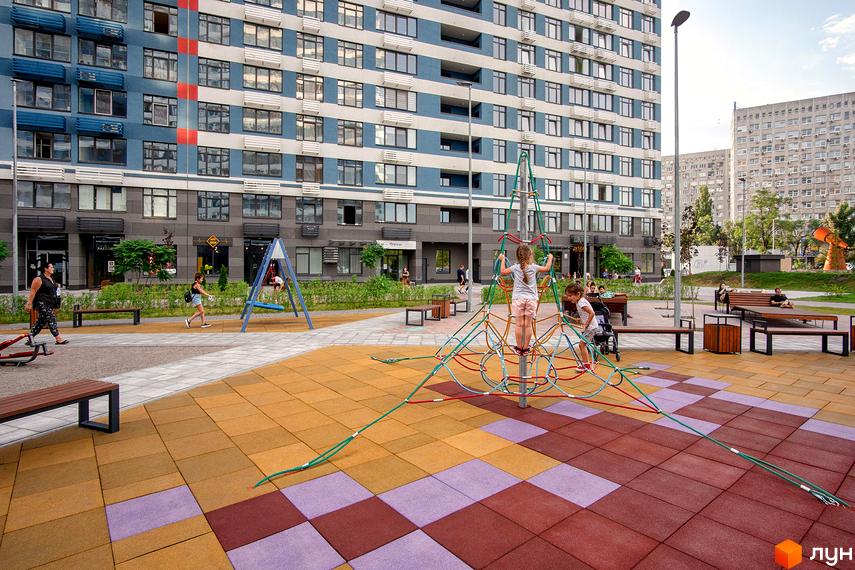 Зовнішній вигляд будинку ЖК Галактика з дитячим майданчиком та зонами відпочинку. Сучасний житловий комплекс з різнокольоровим покриттям та ігровими елементами.